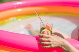 Close-up al unei femei care stă într-o piscină de vară cu o băutură răcoritoare din fructe